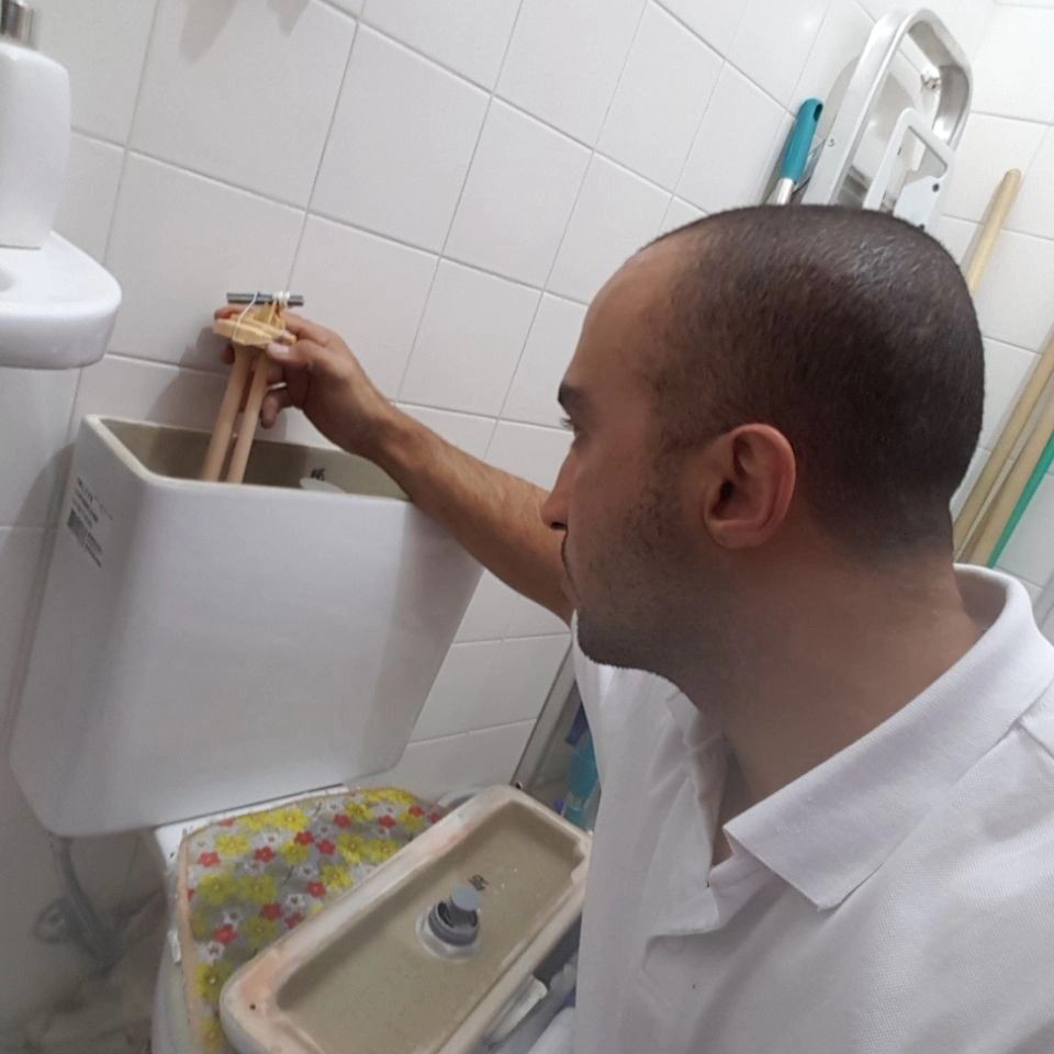Person inspecting and repairing the inside of a toilet tank in a tiled bathroom.